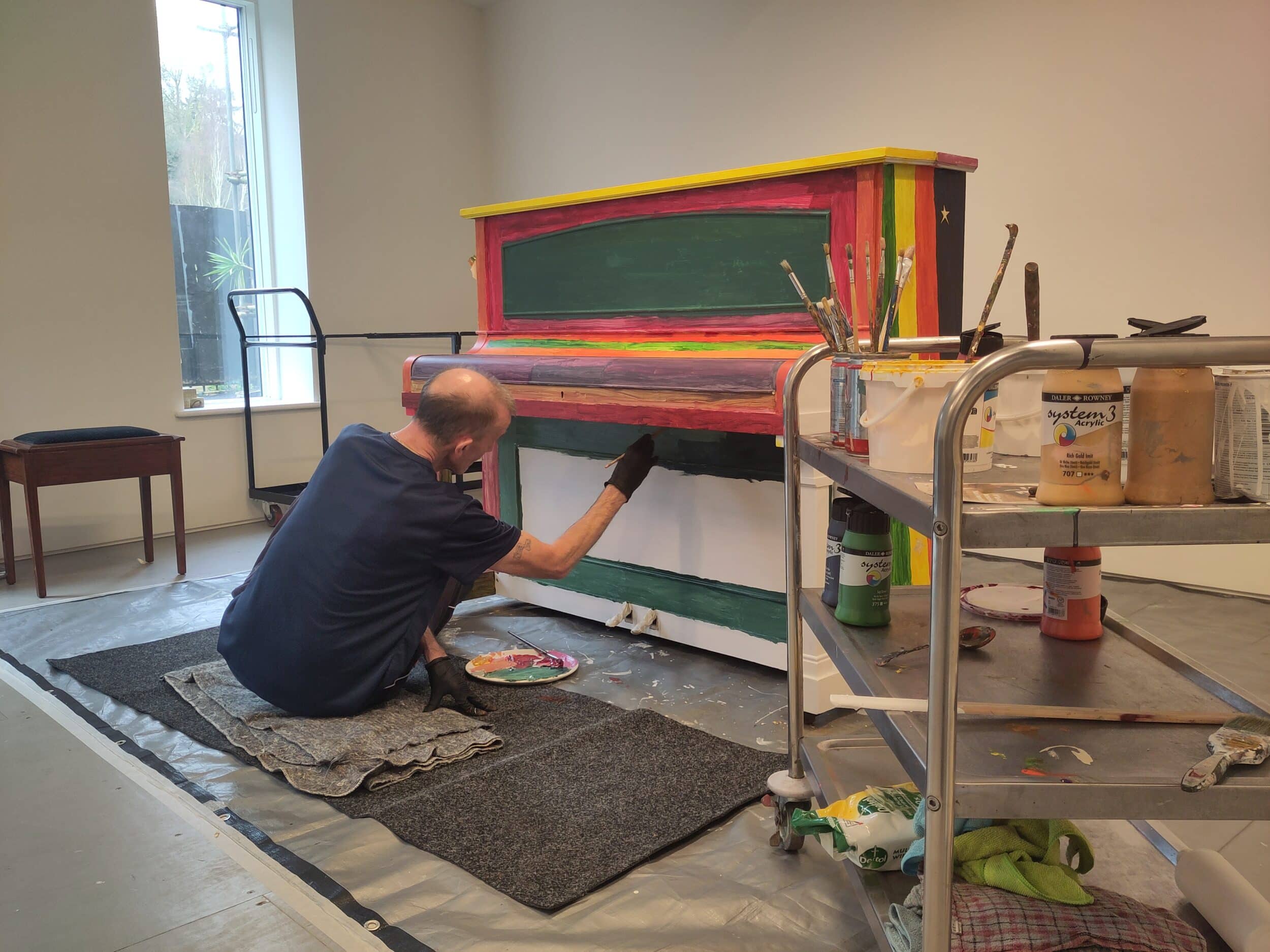 Mark decorates a piano in the studio. He is painting the piano in bright bold colours.